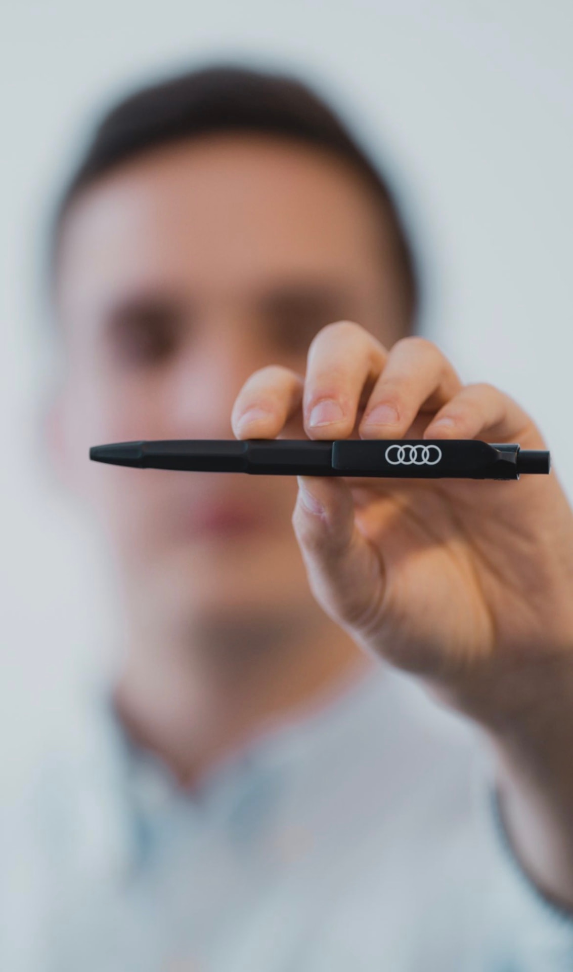 Person holding a black ballpoint pen printed with the Audi rings logo